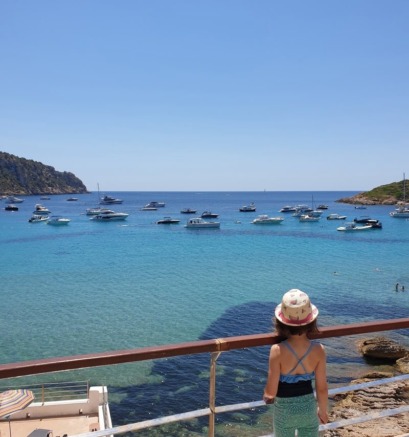 kleines Mädchen im Mallorca Urlaub mit Sonnenhut schaut auf das Mittelmeer und einige Yachten
