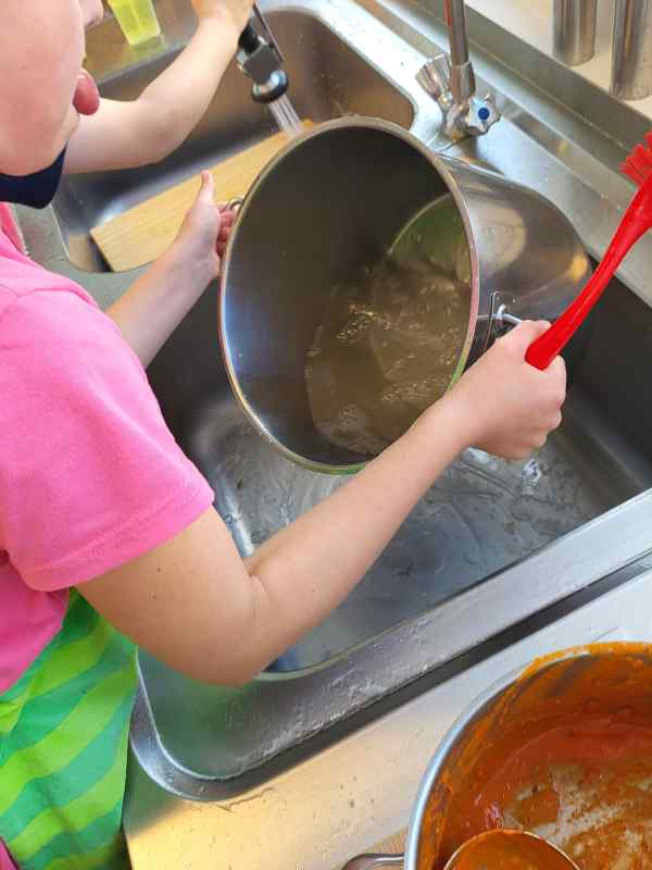 Kinder spülen im Kinderkochkurs Töpfe an Abwaschstation